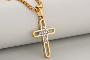 Détail du pendentif croix évidé en acier doré serti de strass brillants sur une chaîne