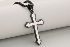 Detalle del colgante de cruz en metal cepillado negro y plata con cadena de caja negra