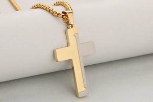 Detailed macro view of two-tone gold and silver stainless steel cross pendant with textured finish