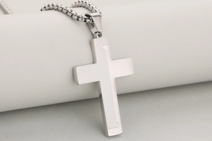 Macro detail of a two-tone cross pendant with diagonal textures and polished silver finish