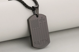 Dettaglio macro della piastrina in acciaio nero con motivo bandiera a croce e incisione Faith