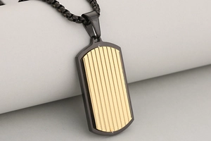 Dettaglio del ciondolo dog tag dorato con texture ondulata e cornice in metallo nero