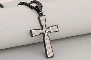 Macro shot of black stainless steel cross pendant featuring engraved Lord's Prayer text