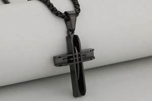 Detail view of a matte black stainless steel cross pendant with a modern industrial layered design