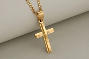 Macro shot of double-layered gold stainless steel cross pendant on a curb chain