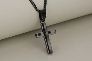 Macro detail of a double-layered black stainless steel cross pendant and cuban chain