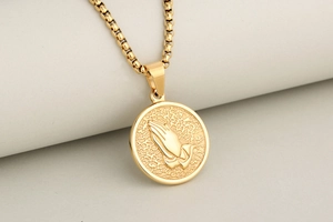 Macro shot of gold praying hands relief on a round medallion with a box chain necklace