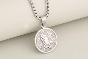 Macro shot of silver stainless steel round coin pendant featuring relief praying hands detail