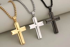 Detailed macro view of three 3D layered stainless steel cross pendants in gold, silver, and black