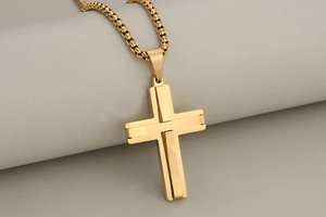 Macro detail of a golden two-layer stainless steel cross pendant on a box chain