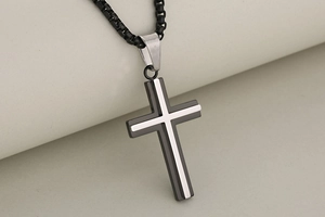 Detail of two-tone stainless steel cross pendant with black and silver layers and box chain