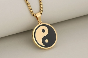 Close-up of golden Tai Chi Yin Yang pendant with polished box chain on fabric background