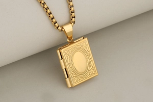 Macro detail of a vintage golden book-shaped locket pendant with wavy textures and box chain