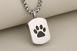 Close-up of a polished stainless steel pet memorial pendant with a black paw print detail