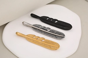 Detailed view of feather-shaped pendants in gold, silver, and black on a white stand
