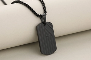 Close-up of black stainless steel dog tag necklace with engraved American flag pattern