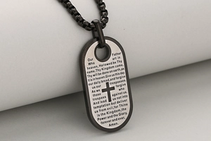 Detailopname van de dog tag hanger met gegraveerd Onze Vader gebed en een kruis