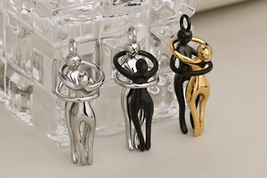 Detalle de colgantes de figuras abstractas abrazadas en acabados plata, negro y oro
