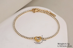 Detalle de pulsera de corazón de cristal dorado con etiqueta de acero y cierre de langosta