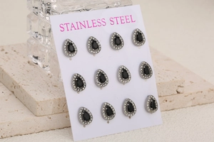 Detail view of twelve stainless steel teardrop earrings with black gems on stone background