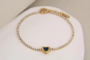 Vista de cerca de pulsera tennis dorada con cristal de corazón azul y circonitas