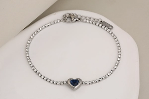 Detalle de una pulsera tenis de acero plateado con una piedra de cristal azul de corazón