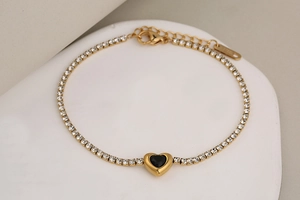 Detalle de la pulsera de acero inoxidable dorado con dije de corazón negro y cristales finos