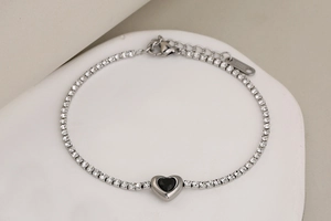 Detalle de una pulsera tenis plateada con corazón negro y cierre de mosquetón