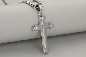Macro view of layered stainless steel cross pendant with cubic zirconia on box chain