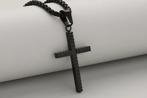 Detalle de colgante cruz de acero negro con textura ondulada y cadena de eslabones cuadrados