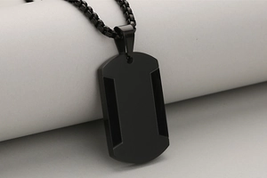 Dettaglio del ciondolo militare nero opaco con bordi geometrici e catena a sfere