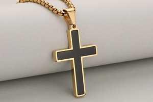 Detail of cross pendant featuring gold finish and black brushed metal inlay texture