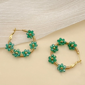 Detail of handmade gold hoop earrings featuring green crystal flowers and beaded petals