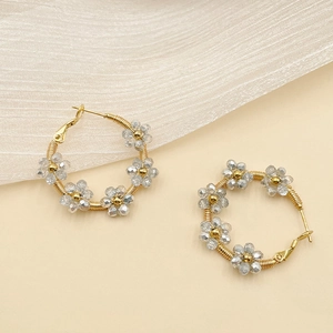 Macro detail of gold hoop earrings with grey crystal beaded flowers on beige background