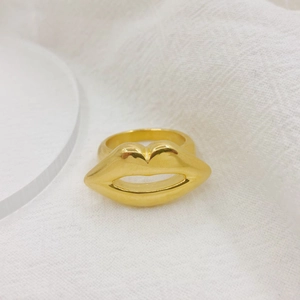 Macro shot of an 18K gold-plated lip-shaped ring on white textured fabric background