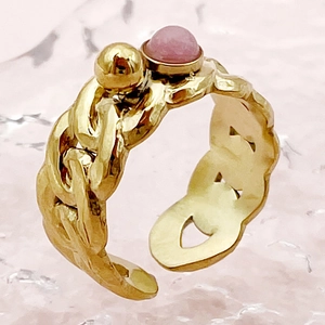 Détail d'une bague chaîne dorée avec une pierre rose sur fond texturé rose poudré