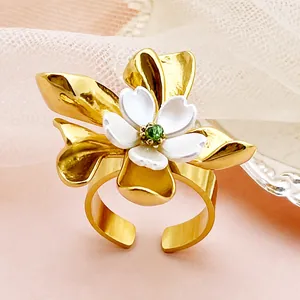 Détail d'une bague fleur dorée avec pétales blancs et gemme verte sur dentelle