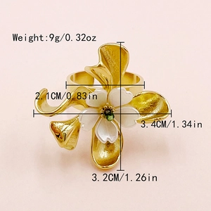 Détail macro d'une bague fleur dorée avec pétales en émail blanc et un centre de gemme verte