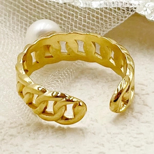 Détail macro d'une bague chaîne dorée avec perle ronde posée sur un tissu texturé blanc