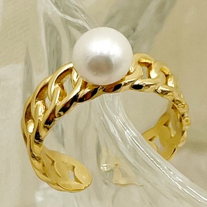 Gros plan d'une bague chaîne gourmette dorée avec perle blanche sur fond de verre texturé