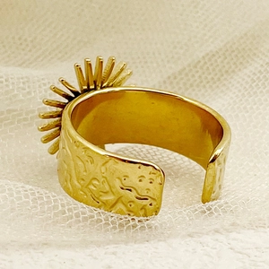 Détail d'une bague fleur dorée avec texture martelée sur fond de dentelle blanche