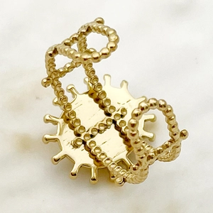 Détail de la bague perlée plaquée or avec motif soleil sur fond de marbre élégant