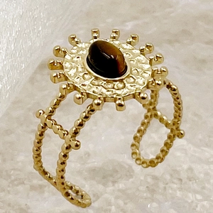 Détail macro d'une bague bohème dorée avec œil de tigre et texture soleil vintage