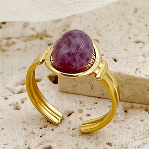 Elegante vergulde open ring met paarse ovale steen op een natuurstenen achtergrond