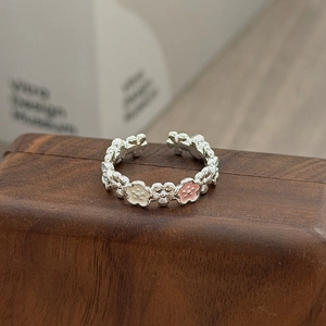 Nahaufnahme eines Vintage-Blumenrings mit rosa Emaille-Blüten auf dunklem Holzgrund