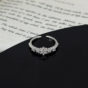 Macro shot of silver zircon star leaf ring on black reflective surface with book background