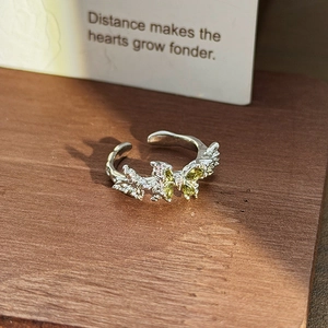Detail of silver adjustable ring with olive green gemstone butterflies on a wood base