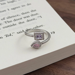 Detail eines verstellbaren Silberrings mit violetten und rosa Steinen auf einem Buch