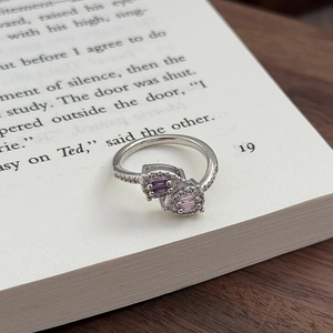 Details des silbernen Bypass-Rings mit lila und rosa Zirkonia auf Buchseiten