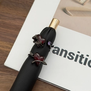Gothic gun black ring set with red heart, arrow, and rose details on a wooden desk